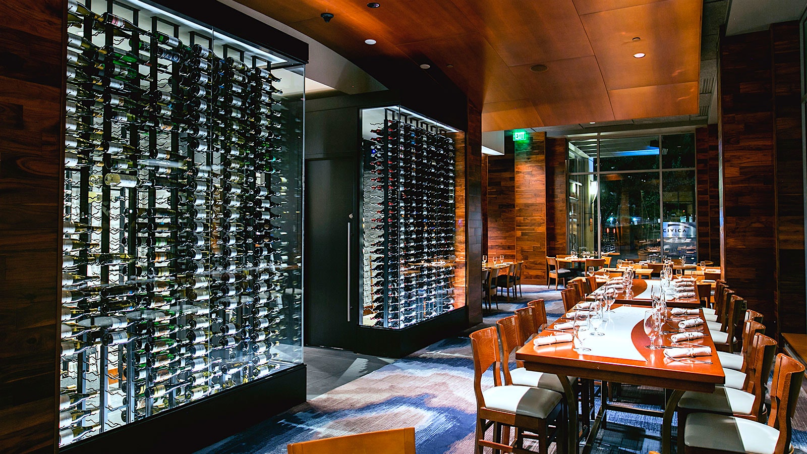  Wooden tables and chairs with white cushions at Seastar Restaurant and Raw Bar, with glass-covered racks of wine bottles and a sleek, modern design throughout